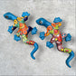 Two colorful talavera gecko wall art pieces on a concrete surface.