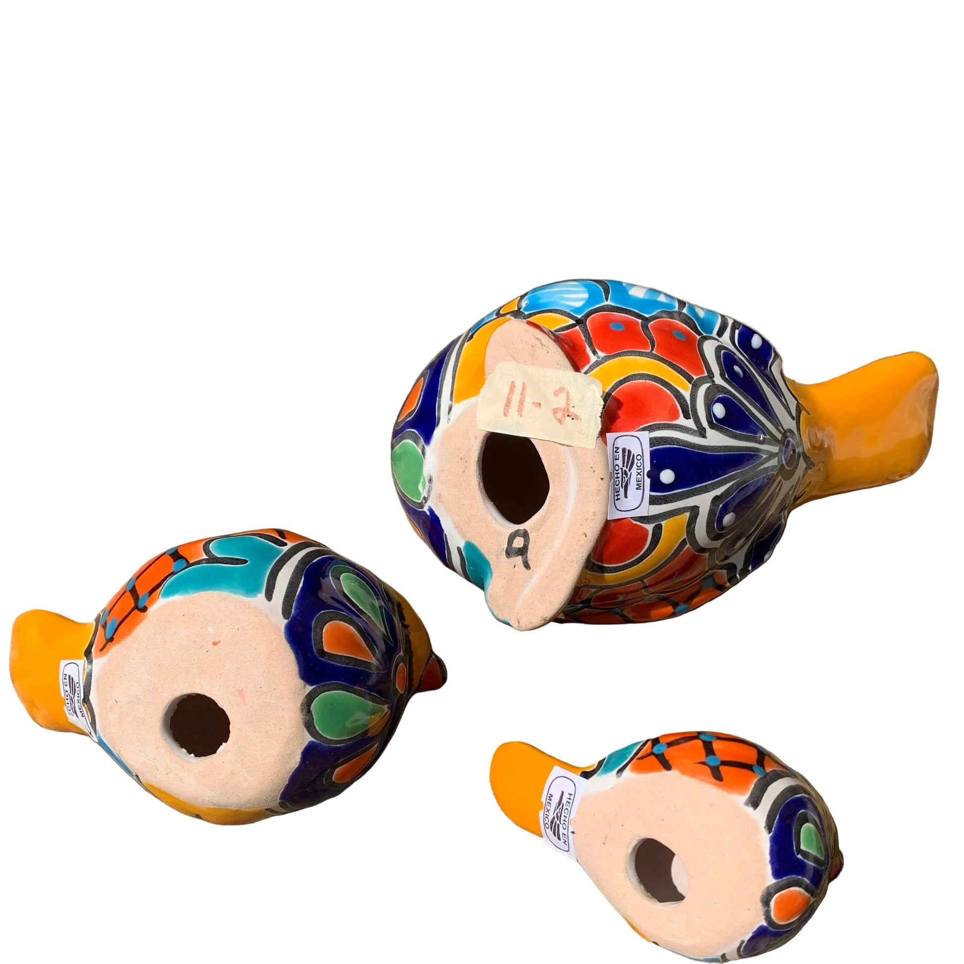 Three hand-painted ceramic bird figurines in yellow, decorated with intricate blue, black, red, green, and orange floral patterns, arranged on a rustic wooden surface bottom view.