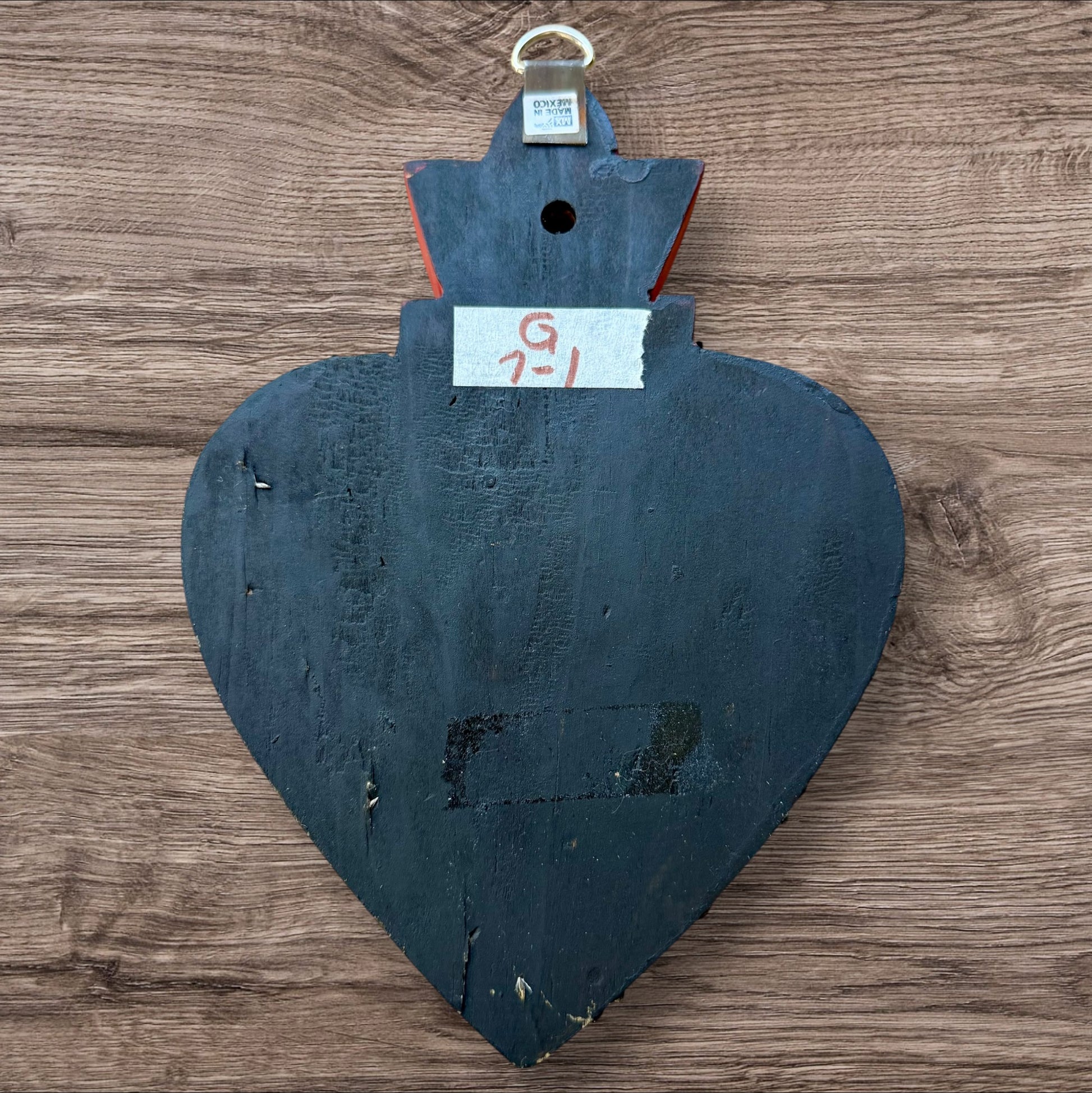 A Mexican Milagros large heart in black with a gold and red flaming top, covered in antiqued charms, back view.