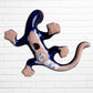A colorful ceramic wall sculpture of a stylized lizard or salamander, decorated with vibrant hand-painted patterns in blue, red, yellow, and orange, mounted on a white brick wall bottom with hanging hole.