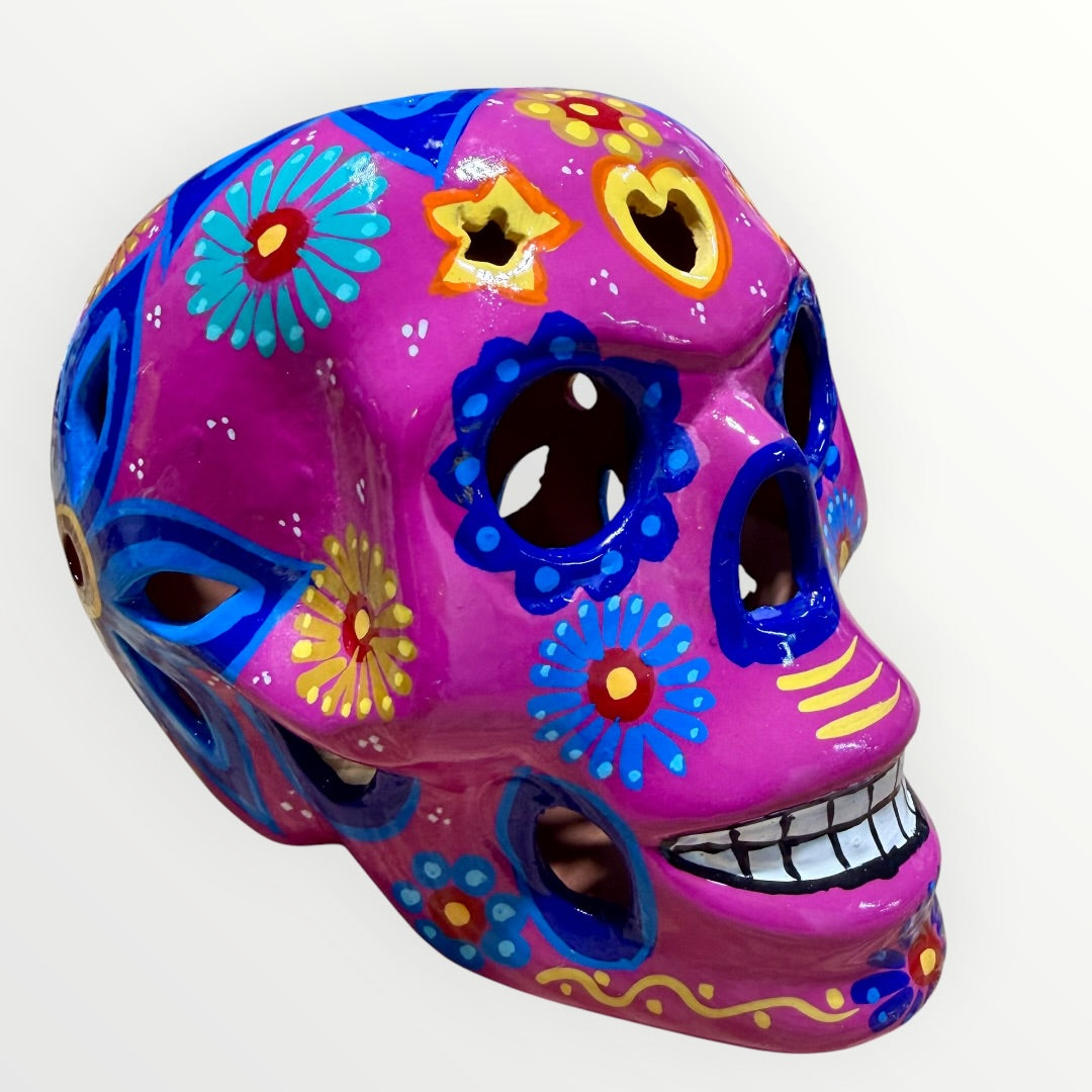 A hand-painted ceramic sugar skull mask in vibrant magenta pink, decorated with colorful floral and geometric patterns in blue, yellow, red, and white, set against a plain white background.