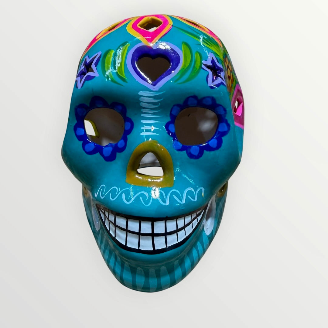 A decorative sugar skull painted in bright turquoise blue with colorful floral and geometric patterns in pink, yellow, green, purple, and white, shown against a plain light background front