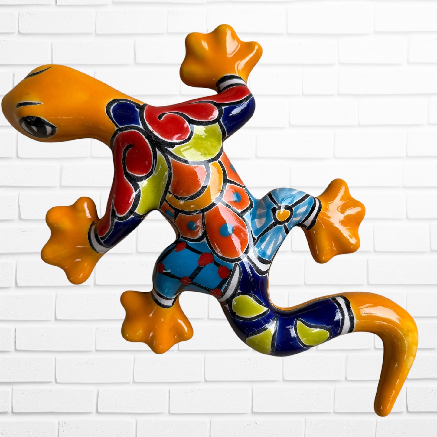 One colorful hand-painted ceramic gecko wall sculpture in a vibrant Mexican folk art style, against a white brick wall.