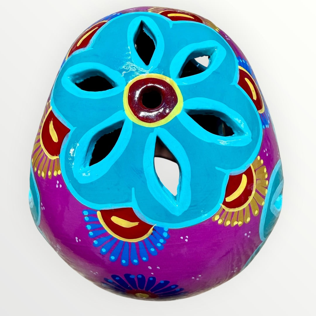A hand-painted ceramic sugar skull in vibrant purple, turquoise blue, and yellow, decorated with floral and geometric patterns on a plain white background top cut out view.