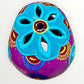 A hand-painted ceramic sugar skull in vibrant purple, turquoise blue, and yellow, decorated with floral and geometric patterns on a plain white background top cut out view.