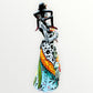 A Day of the Dead Catrina of a Frida skeleton doll holding a black cat, with a red parrot on her shoulder and colorful flowers around the top of her dress. Left side view of the doll.