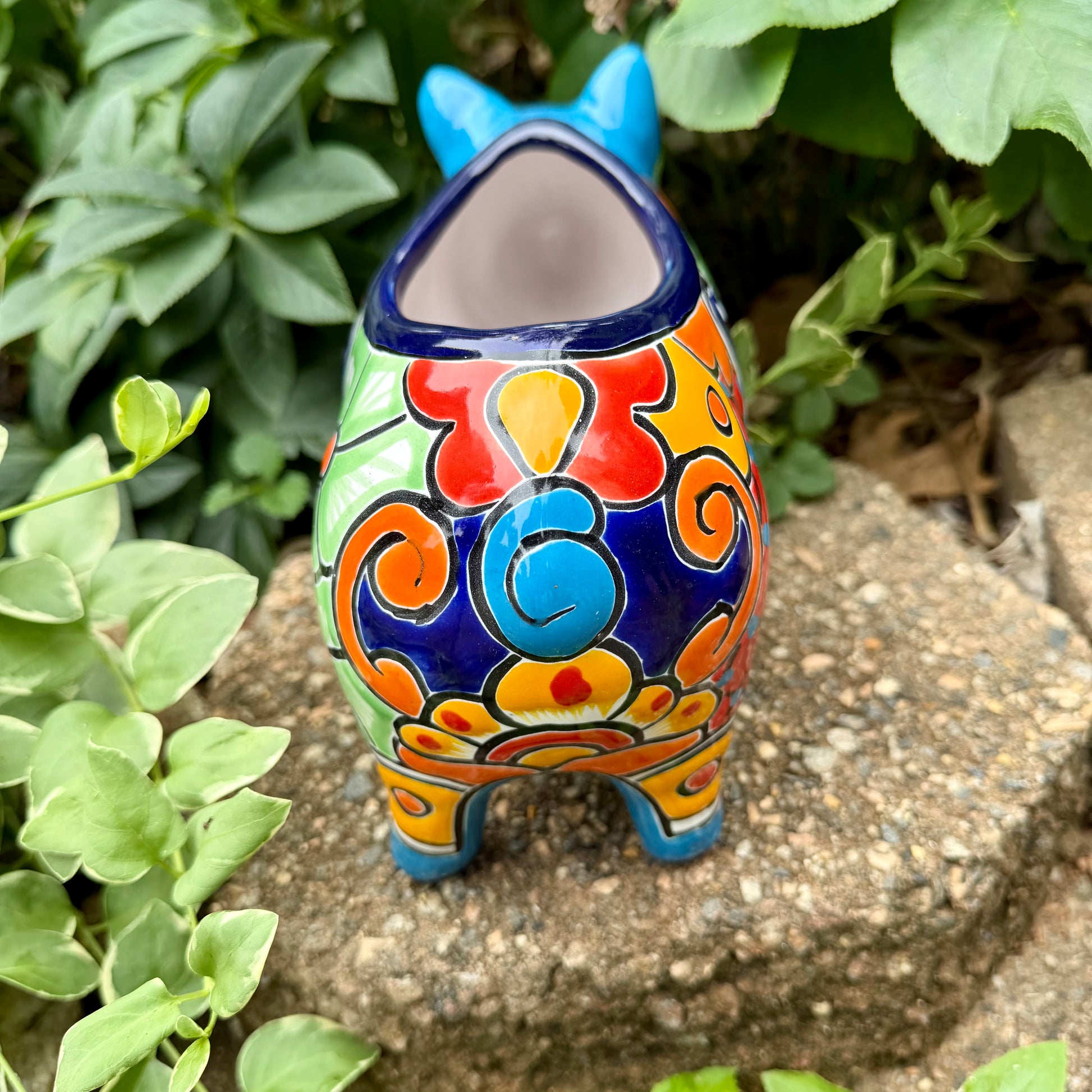 Colorful Talavera ceramic pig planter on a stone surface with green plants in  Back tail view