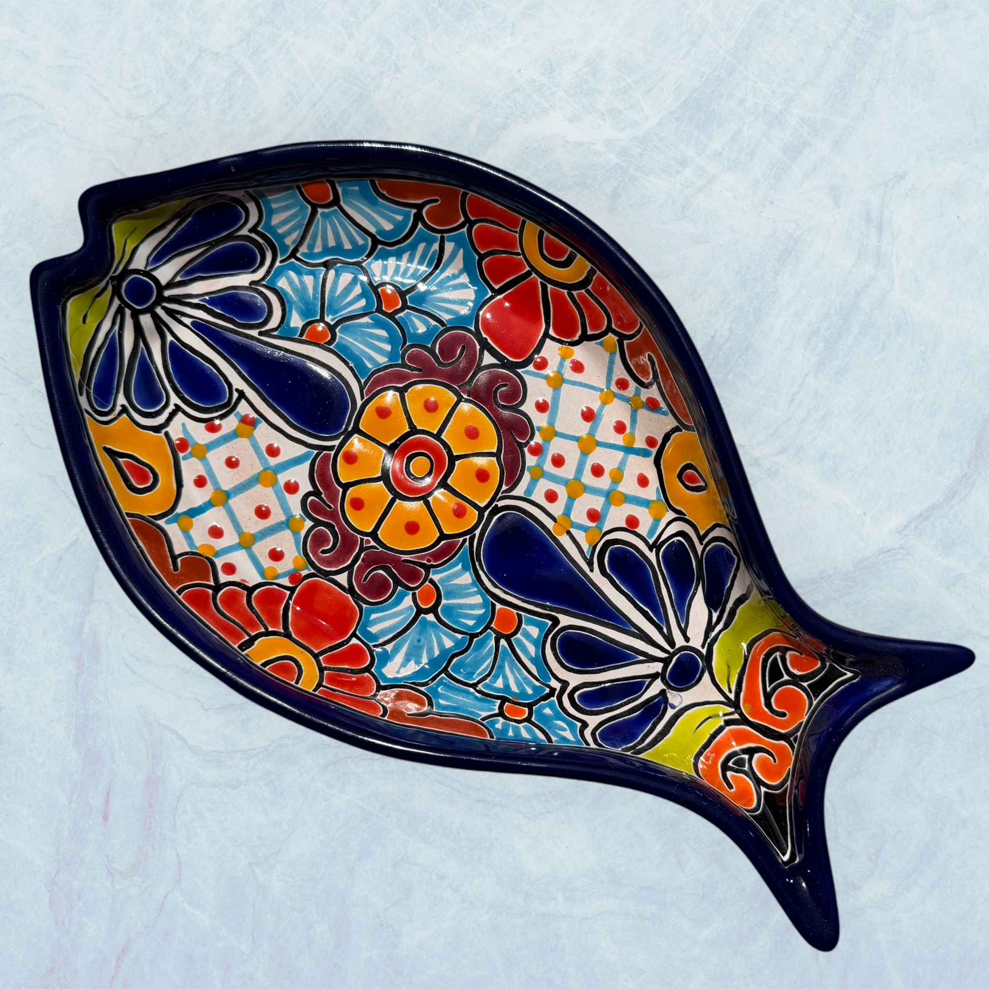 One blue decorative fish-shaped talavera dishes with colorful hand-painted floral patterns, displayed on a light blue textured background.