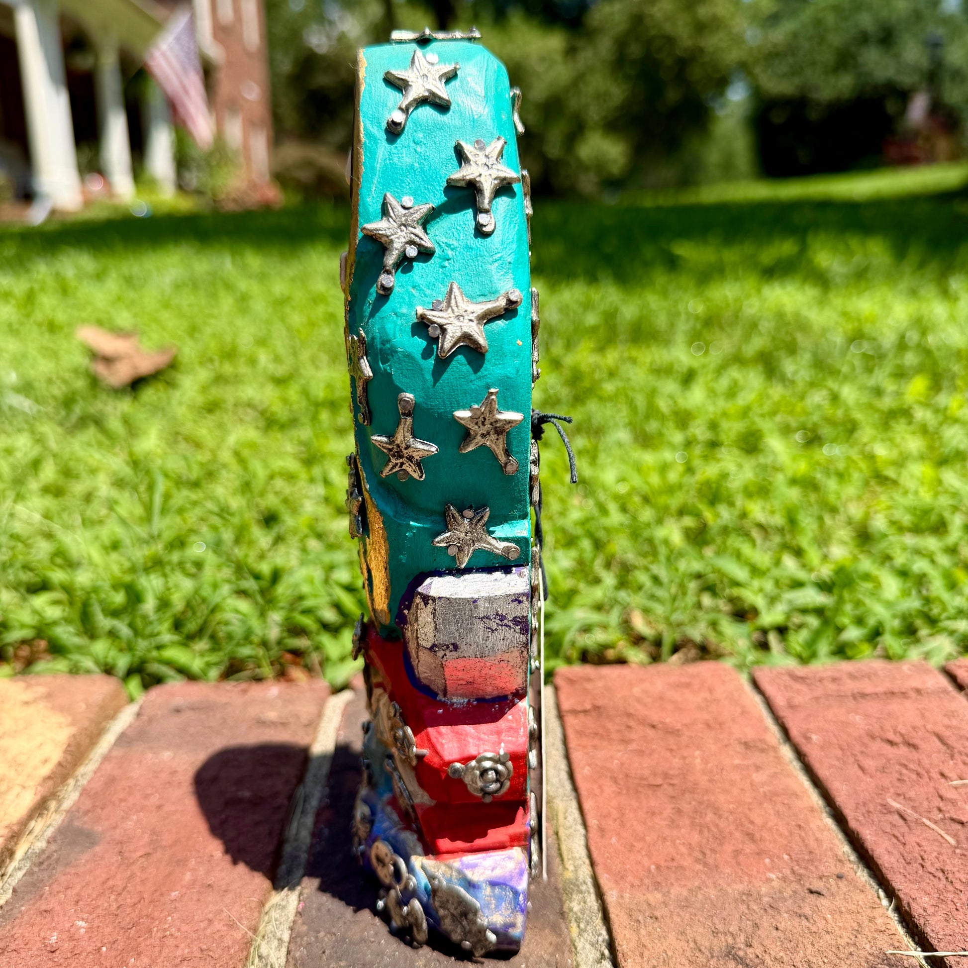 A colorful Milagros Guadalupe  (Virgin Mary) standing on a brick surface outdoors with a grassy yard in the background, right side view.