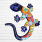 A colorful Talavera ceramic wall sculpture of a salamander, featuring a glossy finish and intricate hand-painted patterns in blue, orange, red, yellow, and white, mounted against a white brick wall.