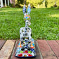 A colorful ceramic donkey Catrina figurine with a skeletal white-and-black design and a floral base, photographed outdoors on a brick surface with a blurred green lawn and house in the background. This is the back view with the tail.