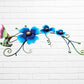Decorative metal wall art with three blue flowers and a colorful hummingbird on a white brick background bottom side view