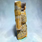 Milagros wooden guardian angel figurine wearing a yellow robe with gold and silver metallic details, standing on a light blue textured background, left side view.