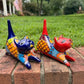 Two colorful ceramic cat figurines, one blue and one red, decorated with geometric patterns, displayed on a brick ledge with a green lawn in the background.