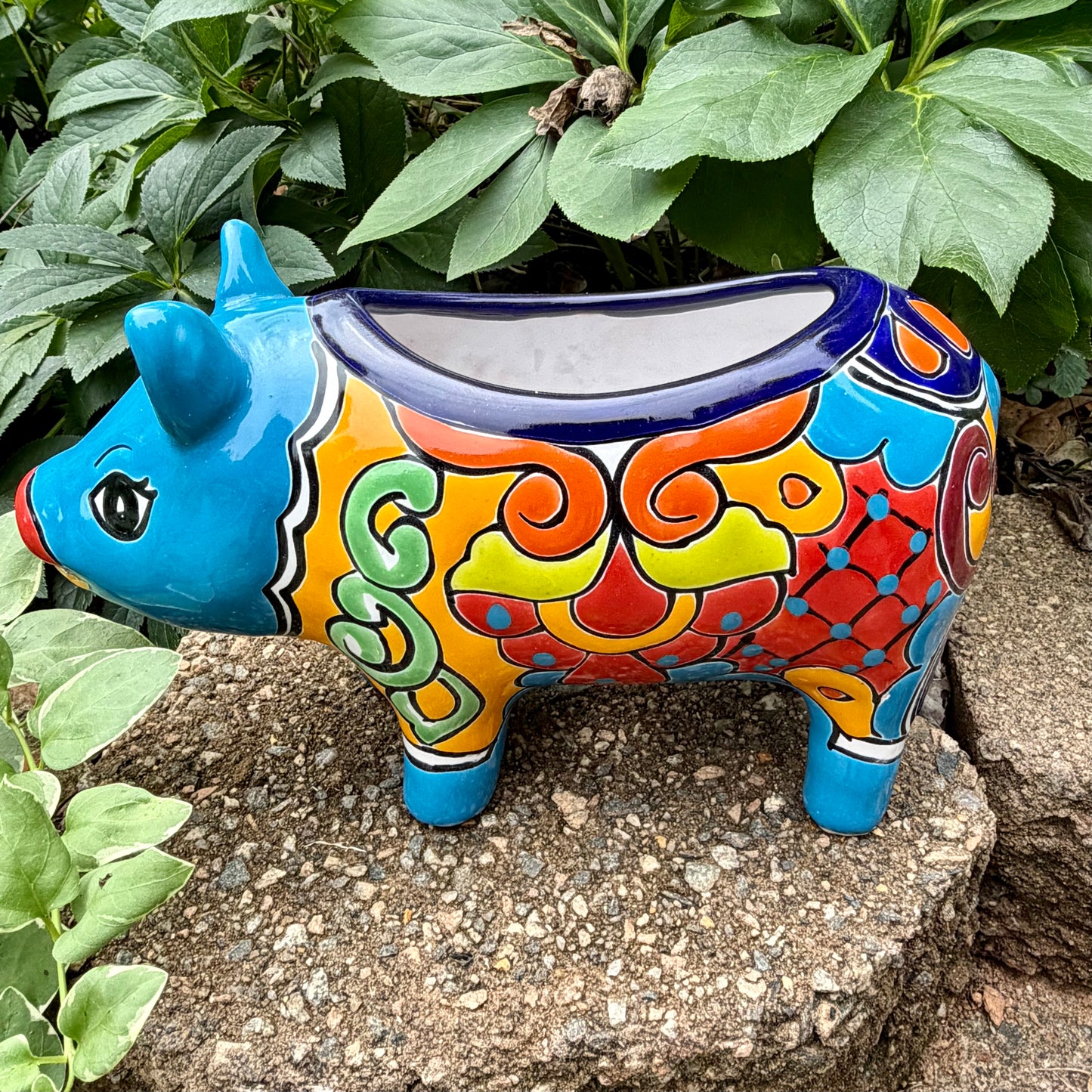 Colorful Talavera ceramic pig planter on a stone surface with green plants in Background right side