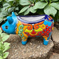 Colorful Talavera ceramic pig planter on a stone surface with green plants in Background right side