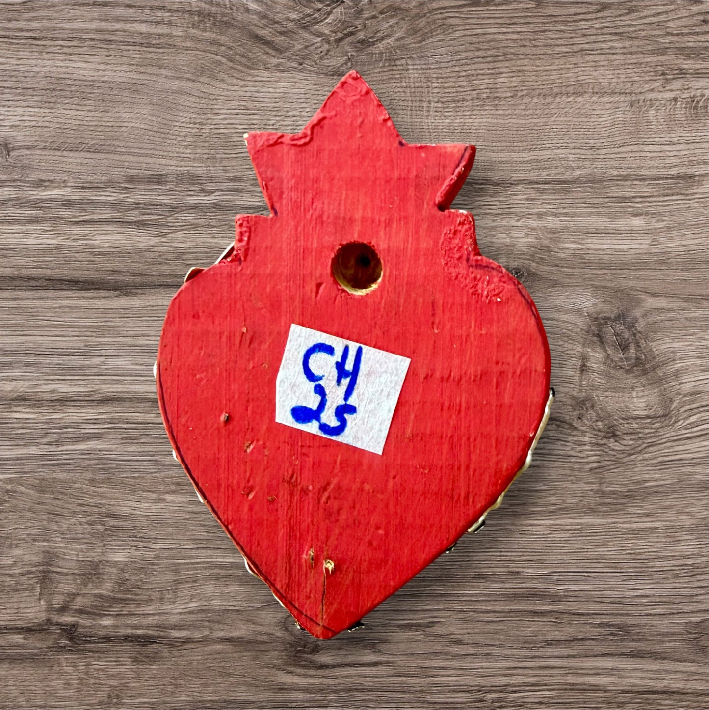 A Mexican Milagros heart in red with a gold flaming top, covered in antiqued charms, back view. 