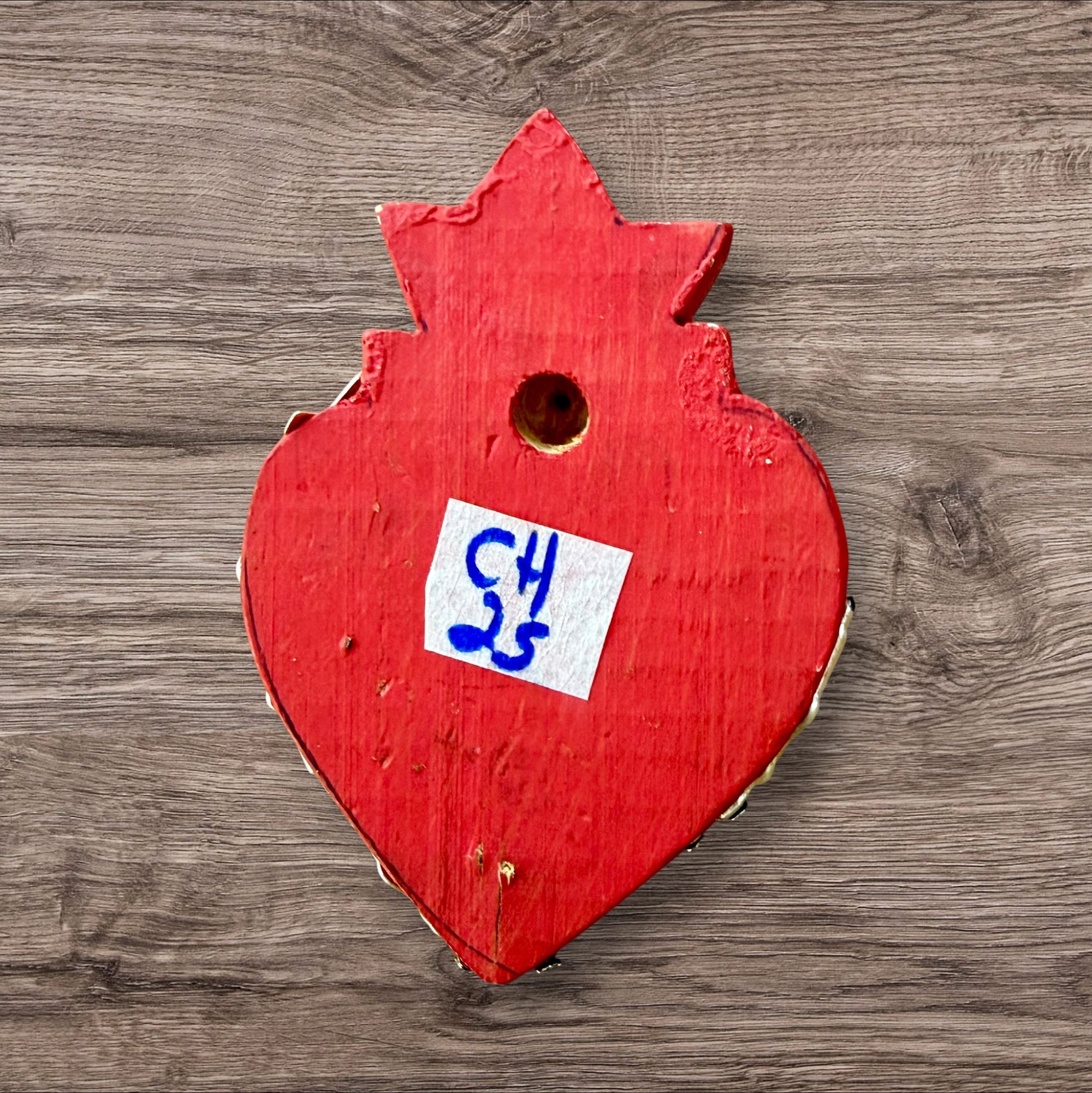 A Mexican Milagros heart in red with a gold flaming top, covered in antiqued charms, back view. 