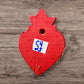 A Mexican Milagros heart in red with a gold flaming top, covered in antiqued charms, back view. 