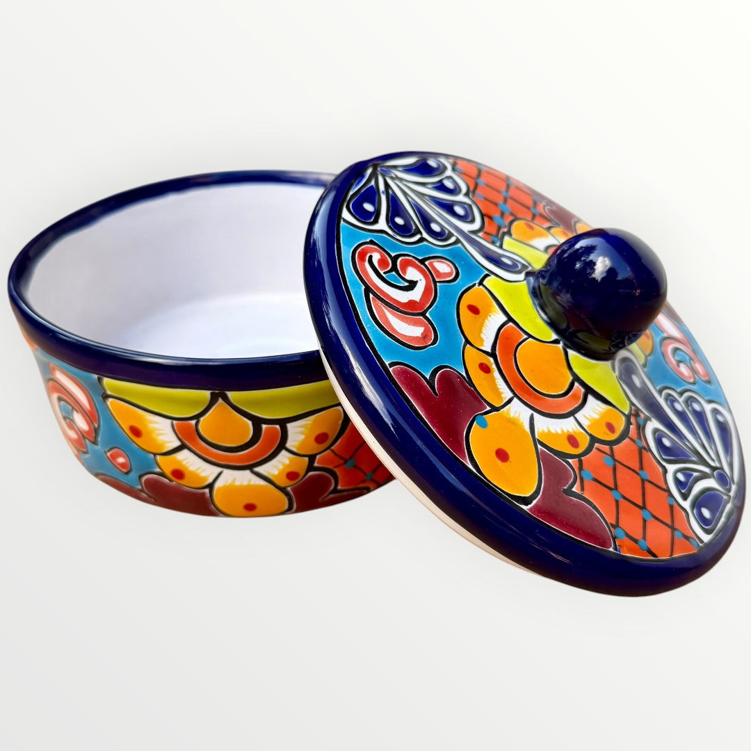 A hand-painted Talavera ceramic lidded container with a colorful Mexican-style floral pattern in blue, orange, yellow, red, and white, featuring a glossy dark blue lid knob. This is the view with cover off.