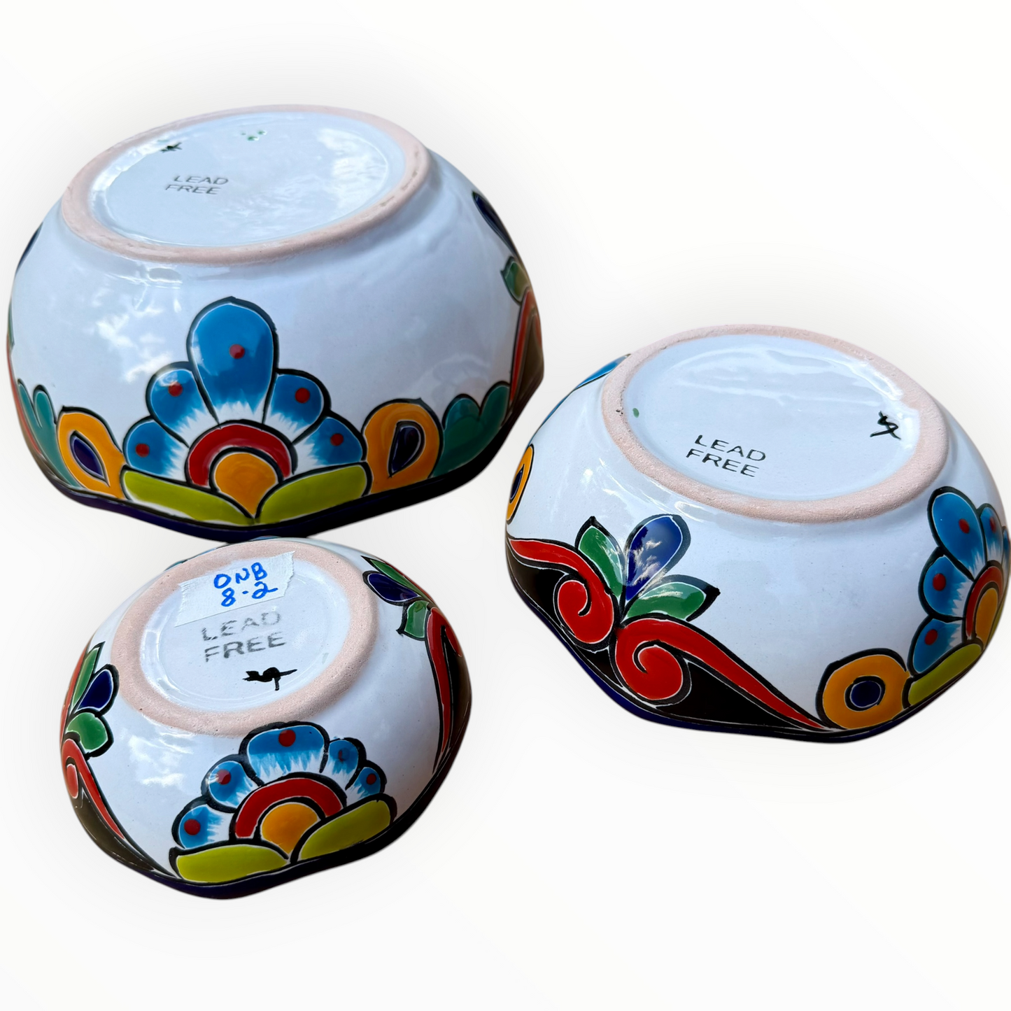 A set of three nested Talavera ceramic bowls with a vibrant hand-painted floral and geometric pattern in multiple colors, featuring a deep blue rim, shown on a plain white background, back side view.