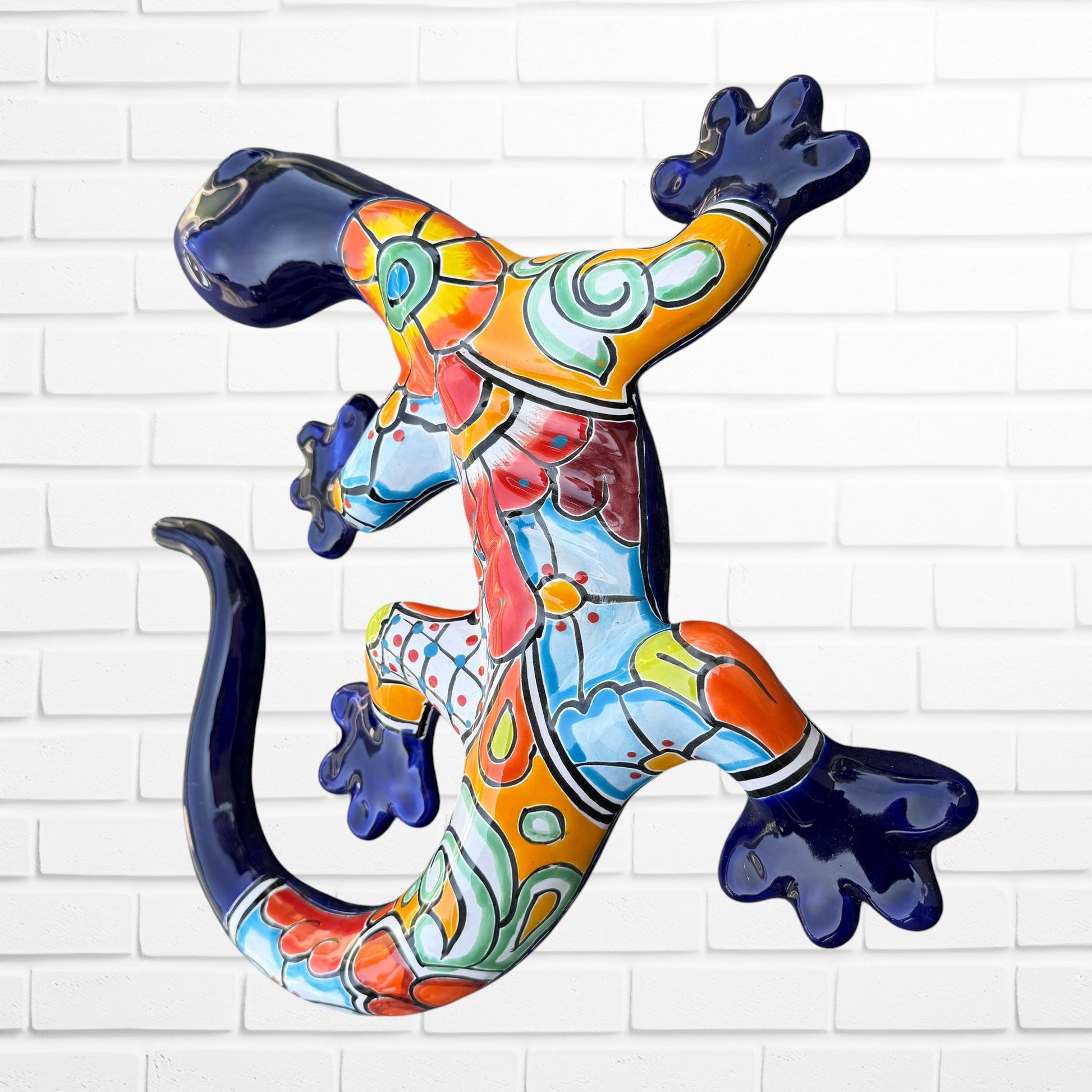 A colorful Talavera ceramic wall sculpture of a salamander, featuring a glossy finish and intricate hand-painted patterns in blue, orange, red, yellow, and white, mounted against a white brick wall, side view of salamander.