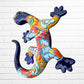 A colorful Talavera ceramic wall sculpture of a salamander, featuring a glossy finish and intricate hand-painted patterns in blue, orange, red, yellow, and white, mounted against a white brick wall, side view of salamander.