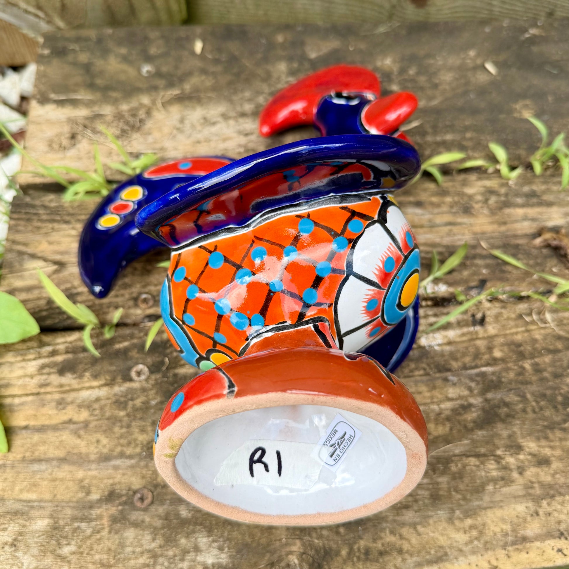 A colorful hand-painted ceramic rooster figurine standing on a rustic wooden surface in front of a green wooden door, bottom of Rooster.