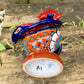 A colorful hand-painted ceramic rooster figurine standing on a rustic wooden surface in front of a green wooden door, bottom of Rooster.