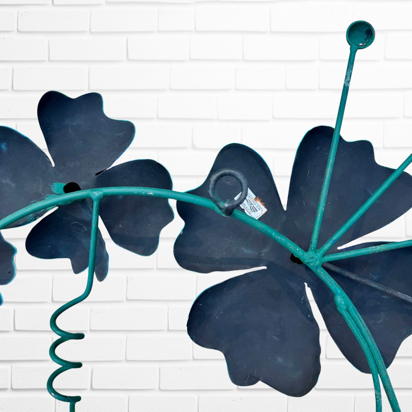 Decorative metal wall art with three blue flowers and a colorful hummingbird on a white brick background hanging loop