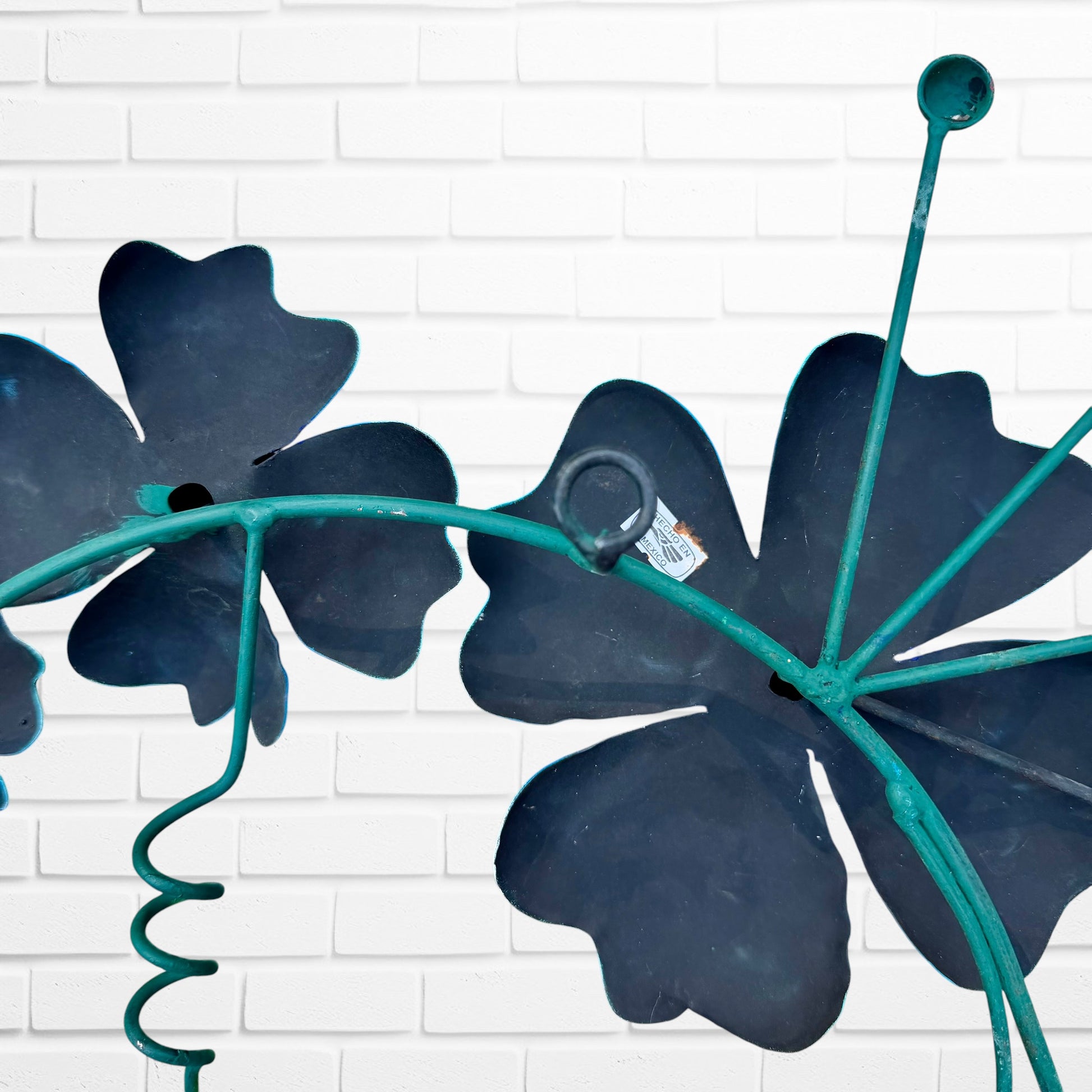 Decorative metal wall art with three blue flowers and a colorful hummingbird on a white brick background hanging loop
