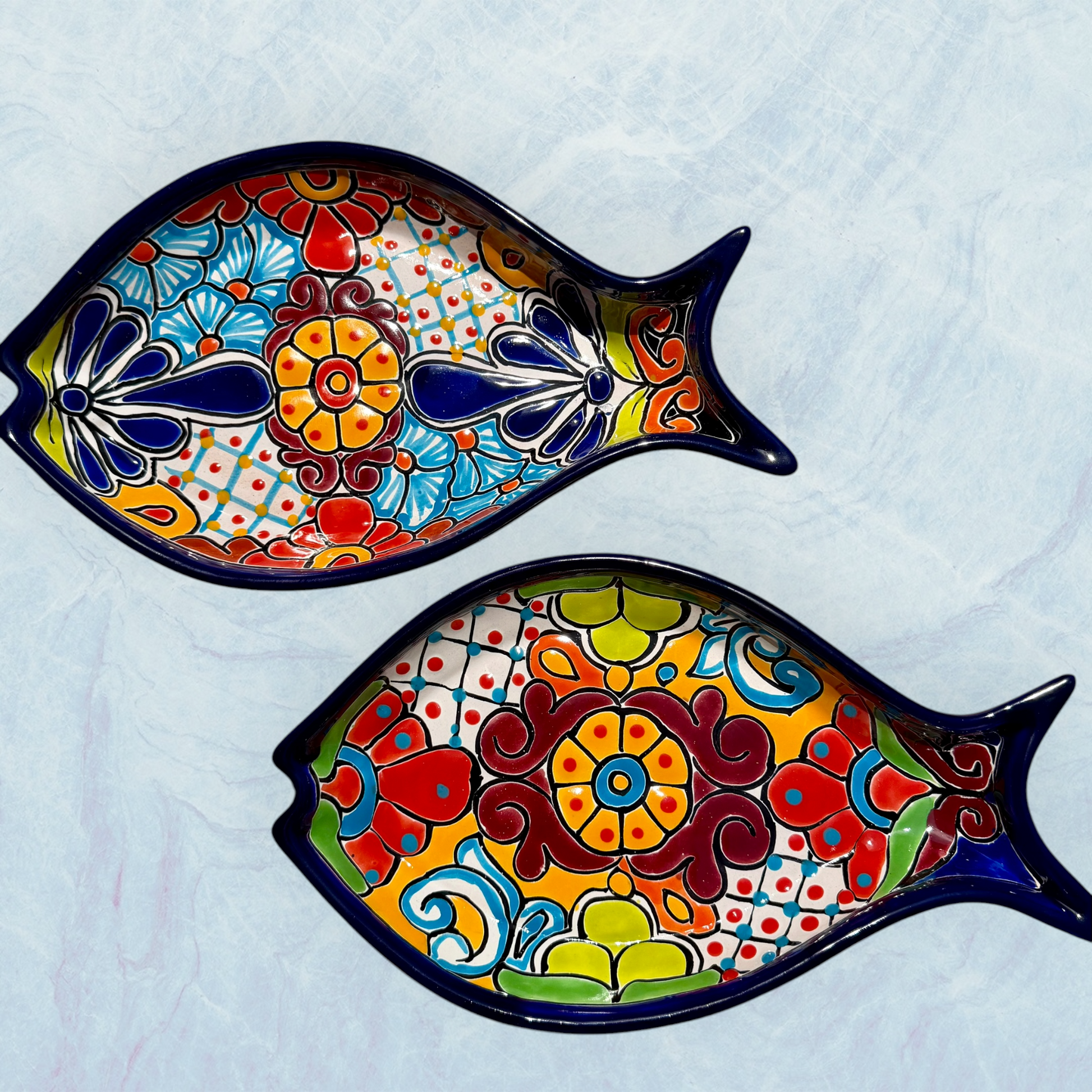 Two blue decorative fish-shaped talavera dishes with colorful hand-painted floral patterns, displayed on a light blue textured background.
