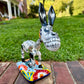 A colorful hand-painted Talavera Catrina donkey figurine, standing on a colorful floral base in an outdoor backyard setting.