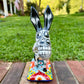 A colorful hand-painted Talavera Catrina donkey figurine, standing on a colorful floral base in an outdoor backyard setting, Front view showing face.