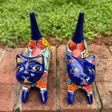 Two cobalt blue with multi-color designs hand-painted talavera ceramic cat figurines resting on a brick ledge with a green grassy lawn top view.