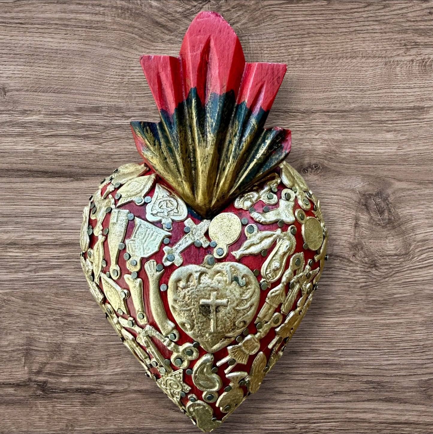 A Mexican Milagros medium heart in red with a gold and red flaming top, covered in antiqued golden charms. #7-1