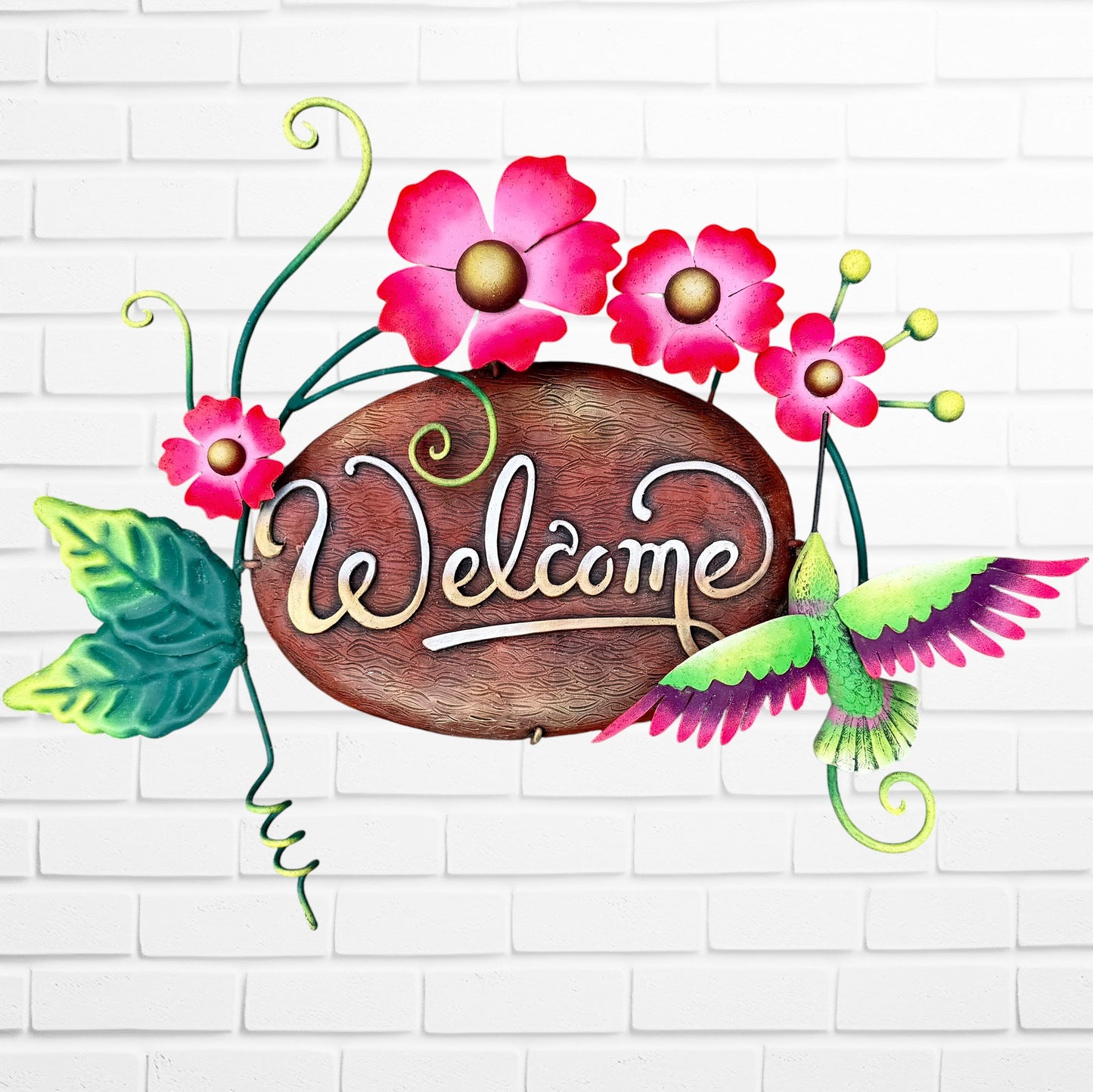 Decorative 'Welcome' sign with pink flowers and a hummingbird on a white brick wall background.
