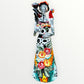A Day of the Dead Catrina of a Frida skeleton doll holding a black cat, with a red parrot on her shoulder and colorful flowers around the top of her dress. Front view of doll.