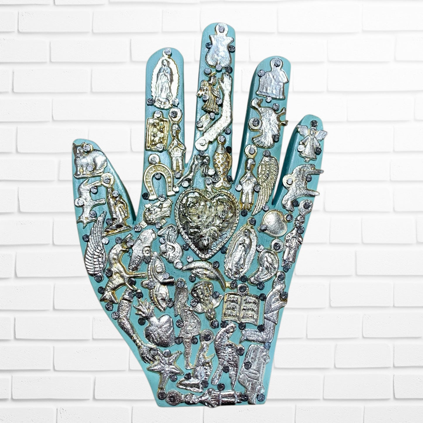 Decorative hand-shaped wall art with various embellishments on a white brick wall background light blue one