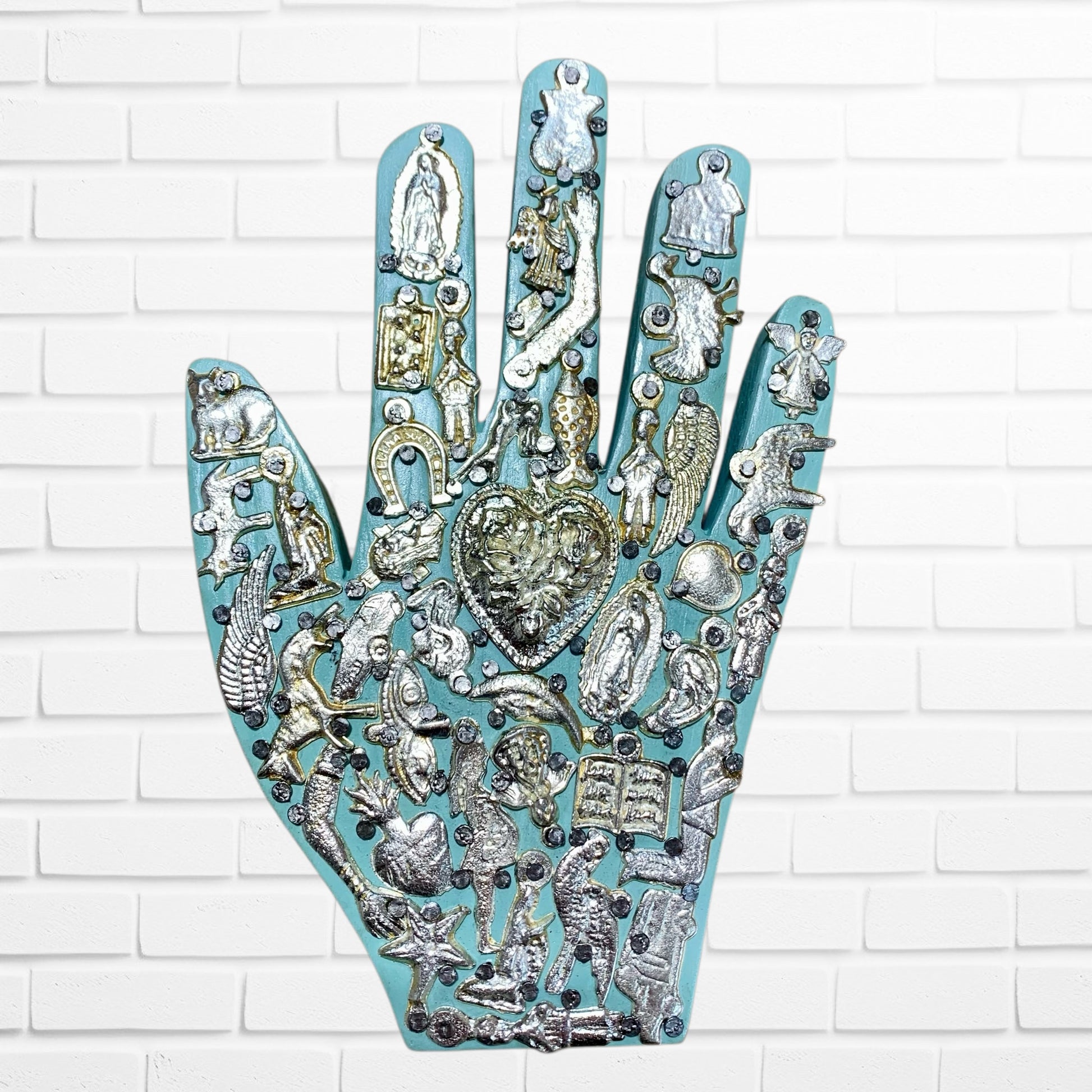 Decorative hand-shaped wall art with various embellishments on a white brick wall background light blue one