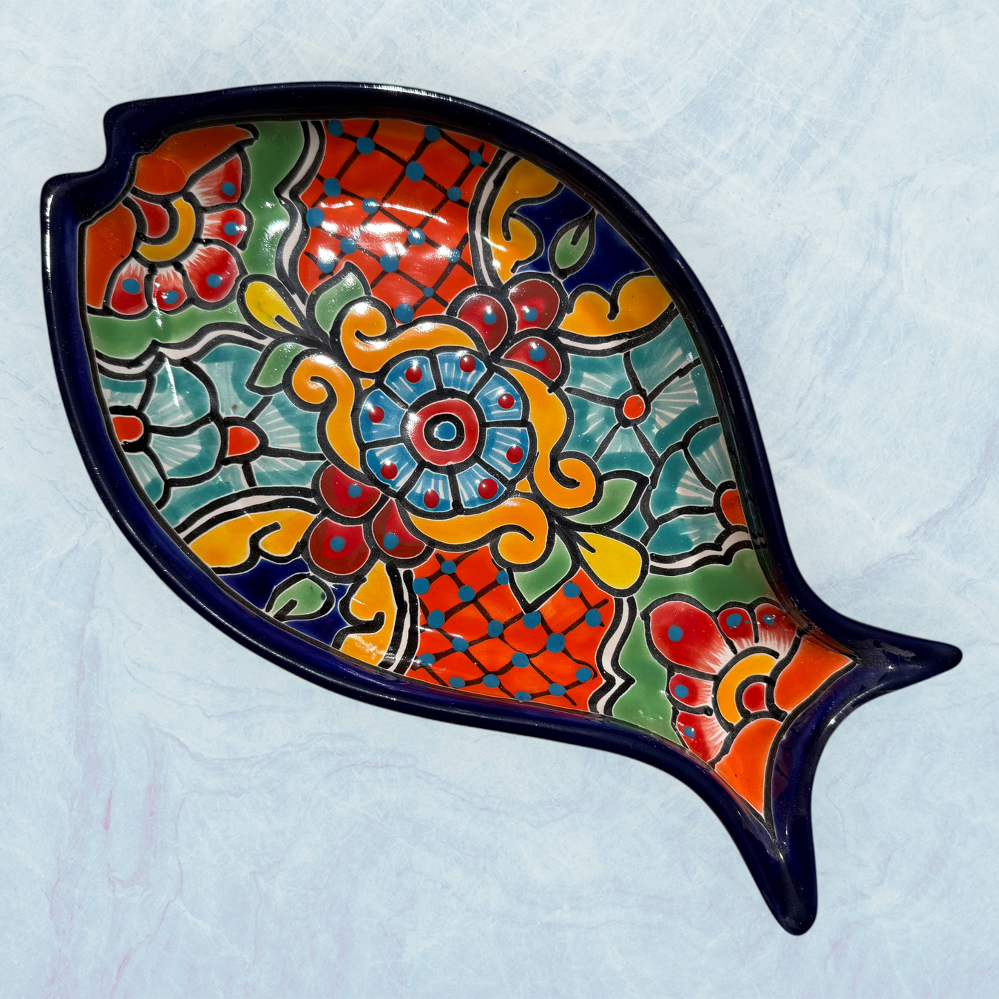 One decorative blue fish-shaped ceramic plates with vibrant hand-painted floral and geometric patterns in red, orange, yellow, green, blue, and purple, set against a light blue background.