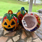Three colorful hand-painted Talavera jack-o'-lantern pumpkins with multi-color displayed on a stone patio with a blurred green lawn background, bottom view.