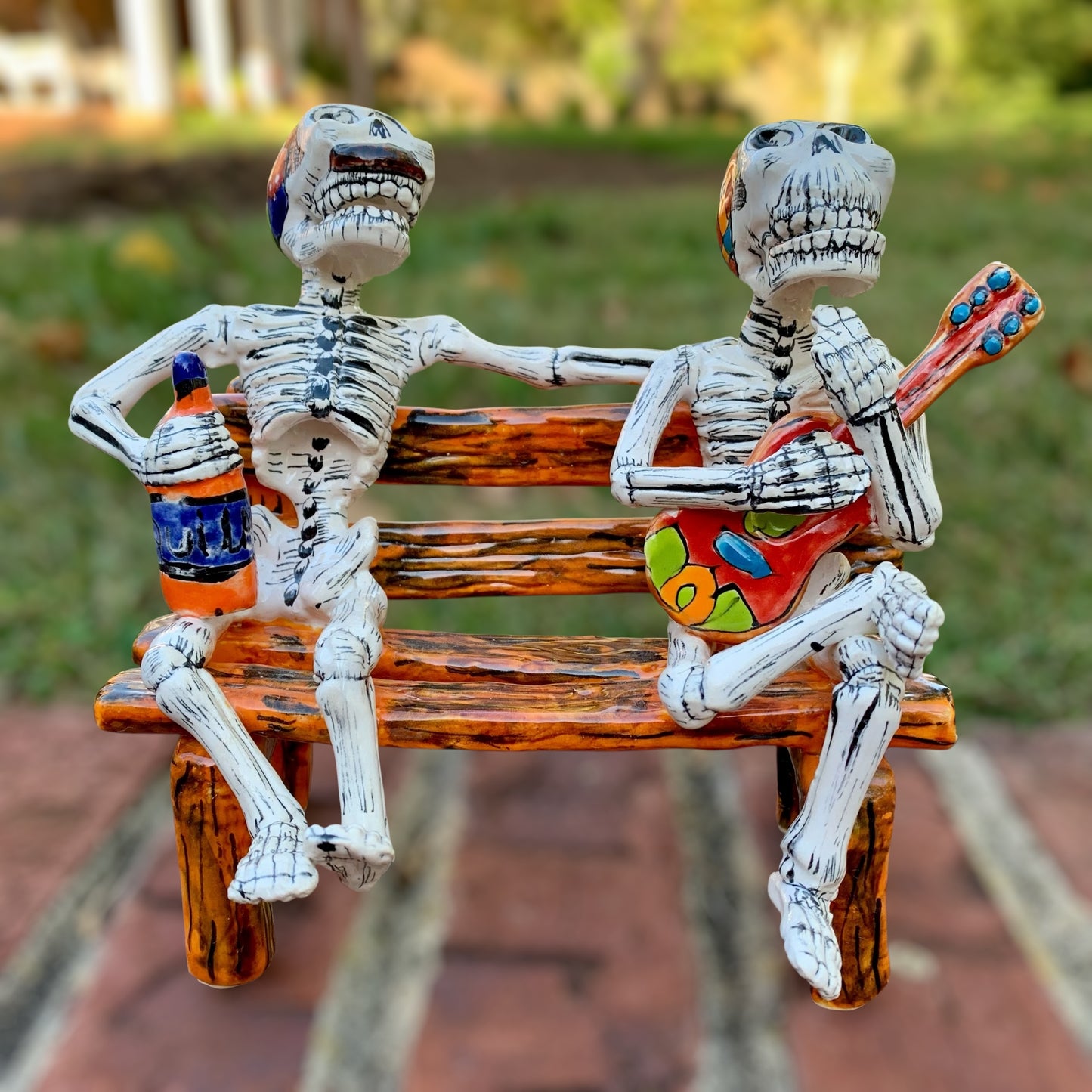 Two skeleton figures sitting on a bench with one playing a guitar and the other holding a bottle.
