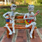 Two skeleton figures sitting on a bench with one playing a guitar and the other holding a bottle.