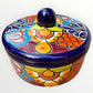 A hand-painted Talavera ceramic lidded container with a colorful Mexican-style floral pattern in blue, orange, yellow, red, and white, featuring a glossy dark blue lid knob.