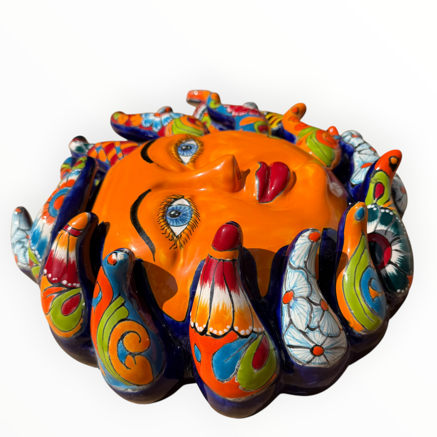 A colorful hand-painted Talavera ceramic sun wall sculpture with big wavy rays on a plain white background, left side view.