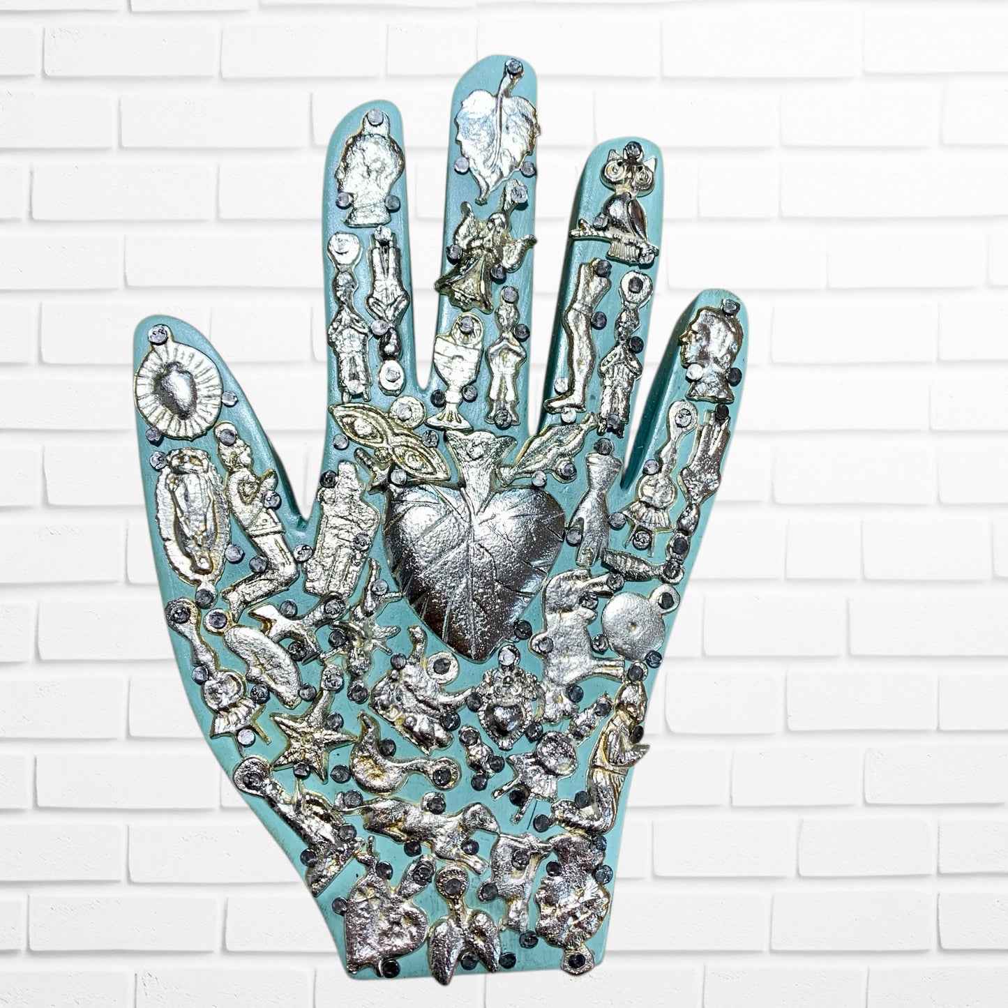 Decorative wall art of a hand with various small figurines and symbols on a white brick background light blue three