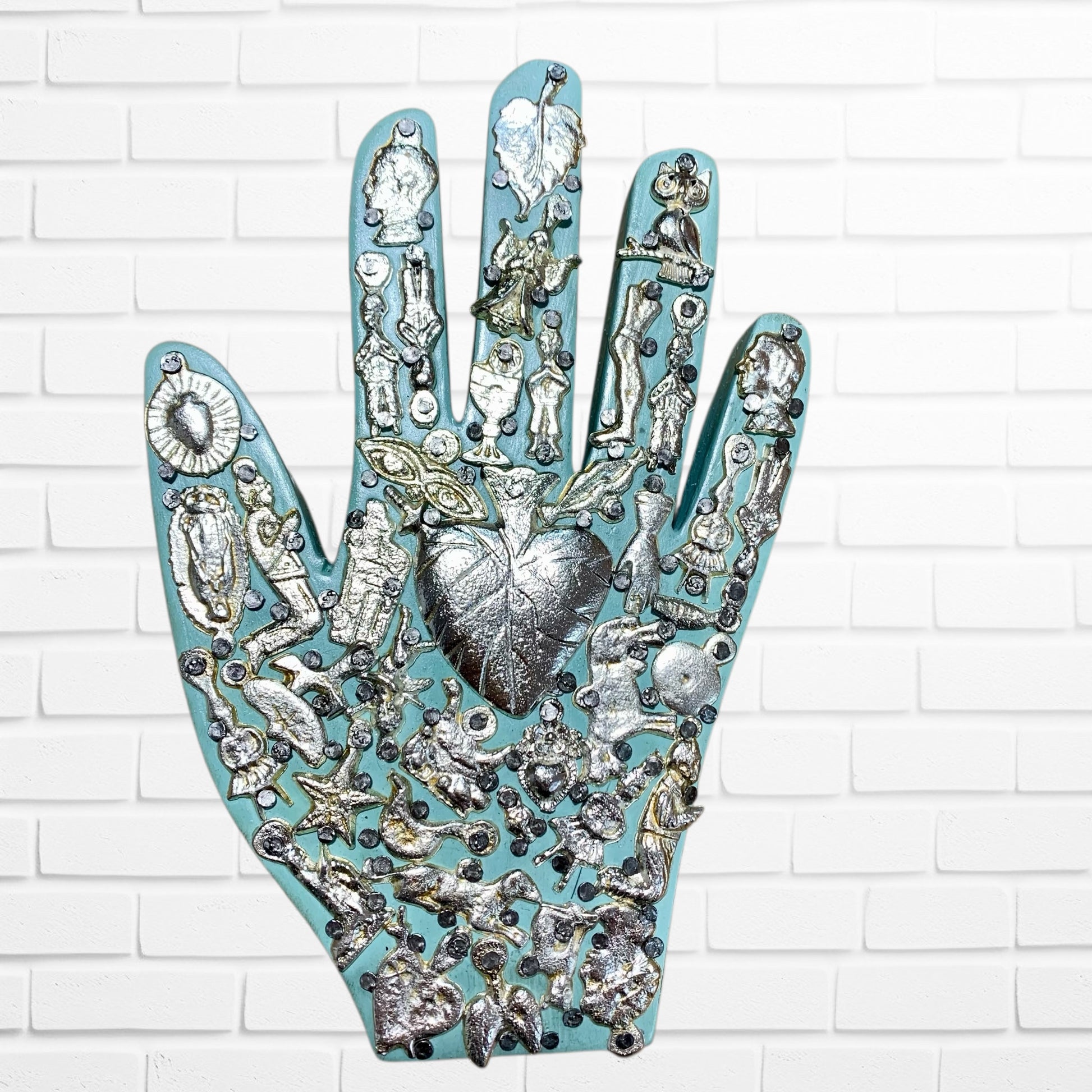 Decorative wall art of a hand with various small figurines and symbols on a white brick background light blue three