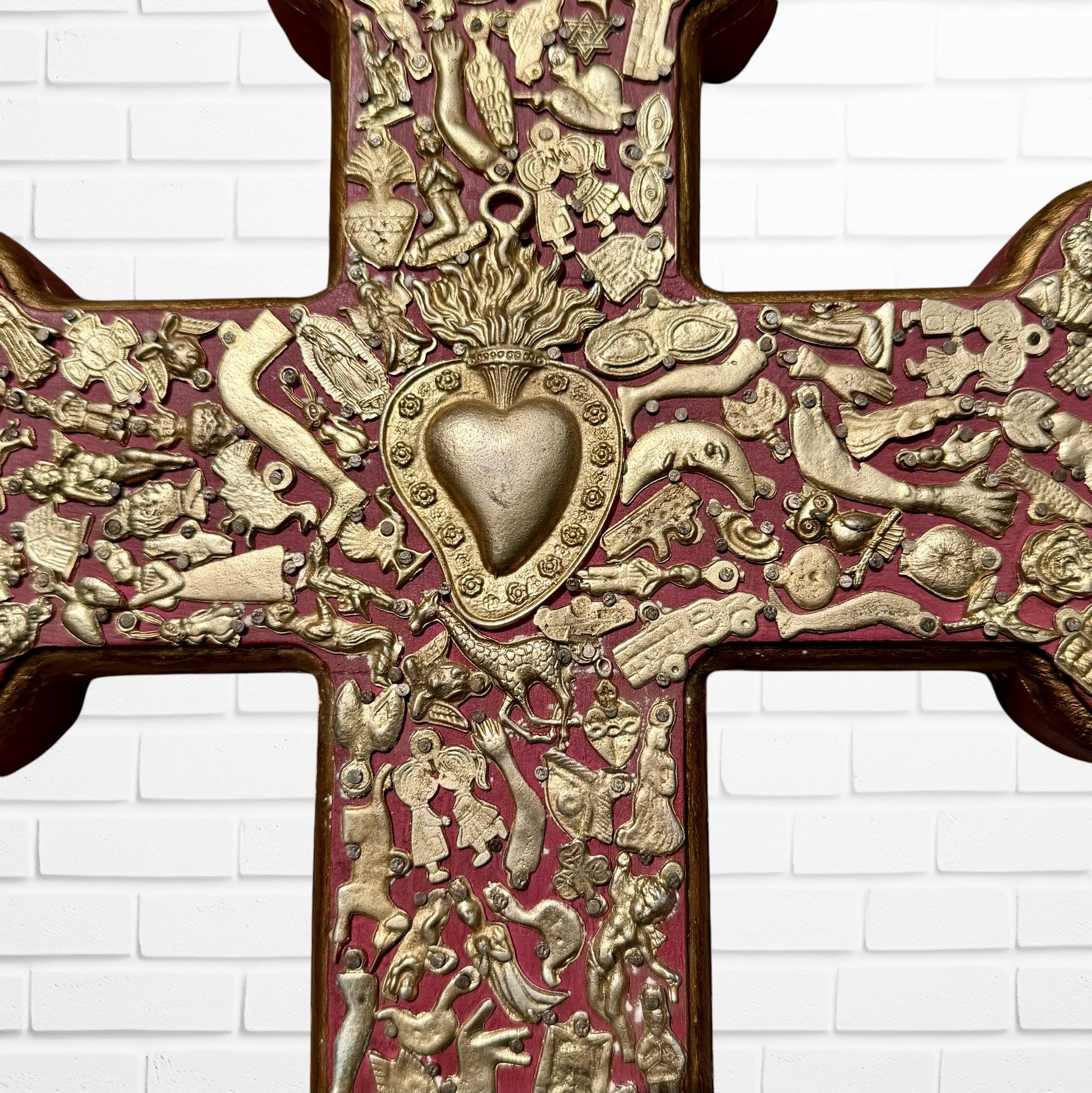 Decorative Milagros wood cross with many charms “miracles” on a white brick wall background Center heart 