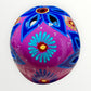 A hand-painted ceramic sugar skull mask in vibrant magenta pink, decorated with colorful floral and geometric patterns in blue, yellow, red, and white, set against a plain white background back skull view.